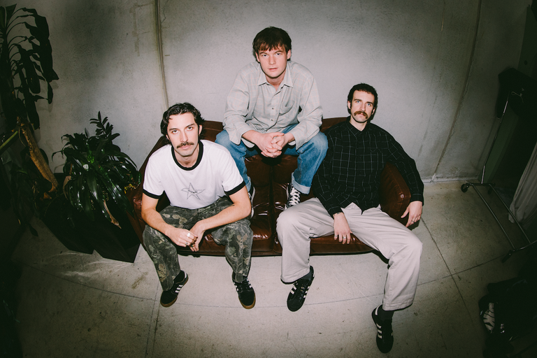 Indie rock band Loose Bricks posing on a leather couch in a wide-angle, fisheye lens promotional band photo.